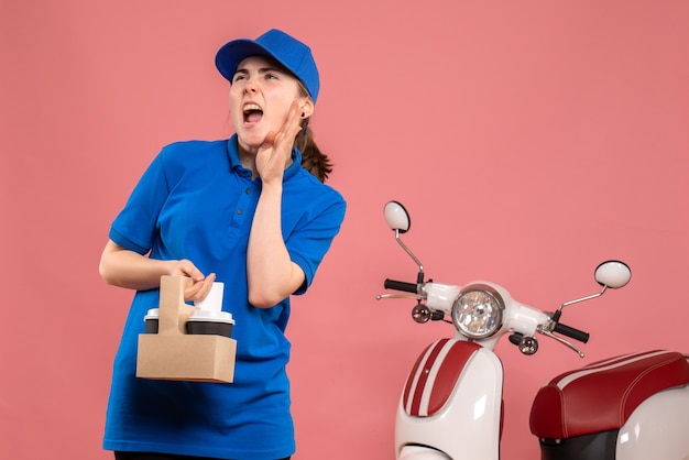 Front view female courier with delivery coffee on the pink work delivery service worker woman bike uniform job