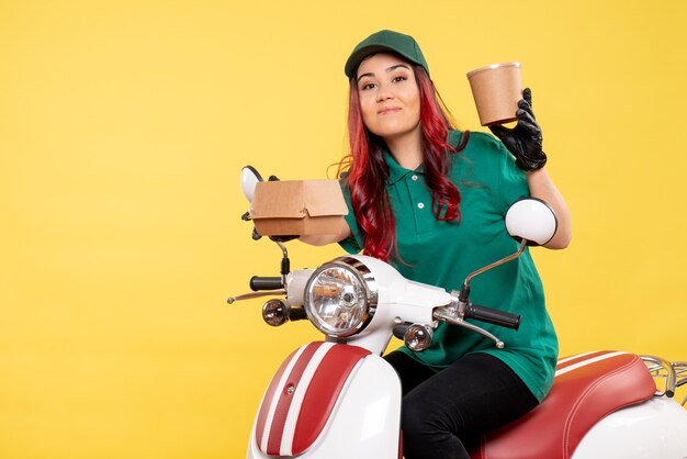 Front view of female courier with delivery dessert and food on a yellow wall