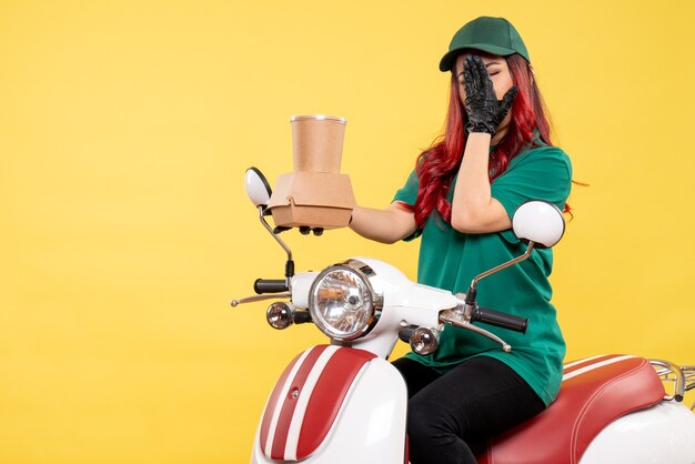 Front view of female courier with delivery dessert and food on the yellow wall