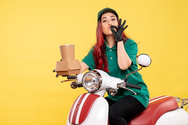 Front view of female courier with delivery dessert and food on yellow wall