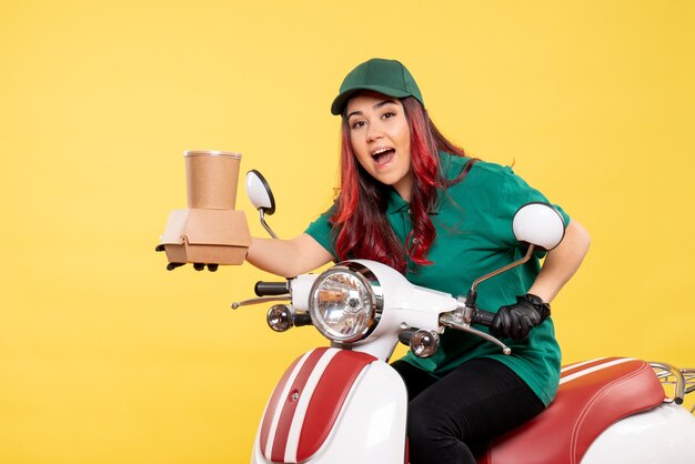 Front view of female courier with delivery dessert and food on yellow wall