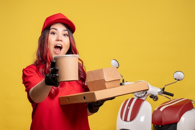 Front view of female courier with delivery food and dessert on yellow wall