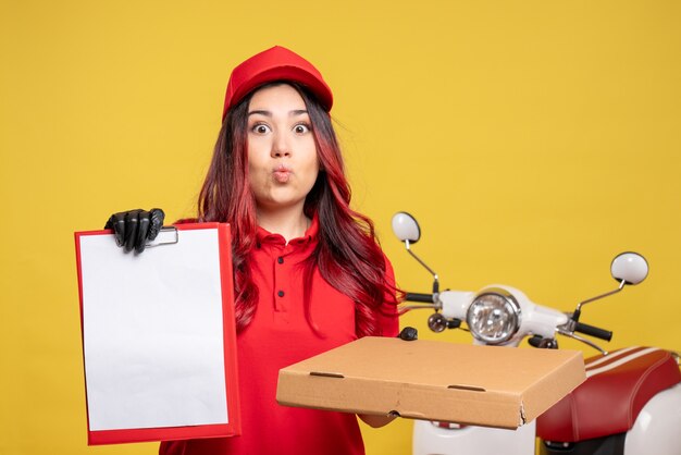 Front view of female courier with food box and file note on yellow wall