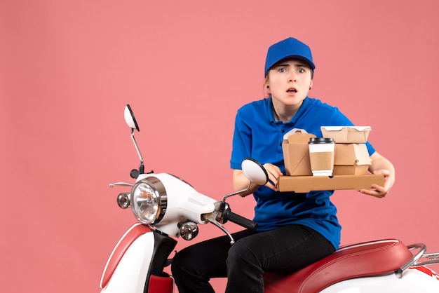 Front view female courier with food packages and boxes on pink job worker food delivery bike uniform service