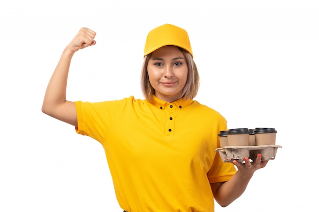 A front view female courier in yellow cap yellow shirt holding coffee smiling on white