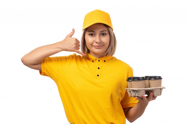 노란색 모자 노란색 셔츠에 전면보기 여성 택배 미소하고 흰색에 포즈 커피를 들고