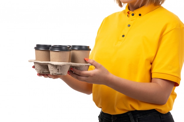 Foto gratuita un corriere femminile di vista frontale in camicia gialla e jeans neri che tengono le tazze di caffè su bianco