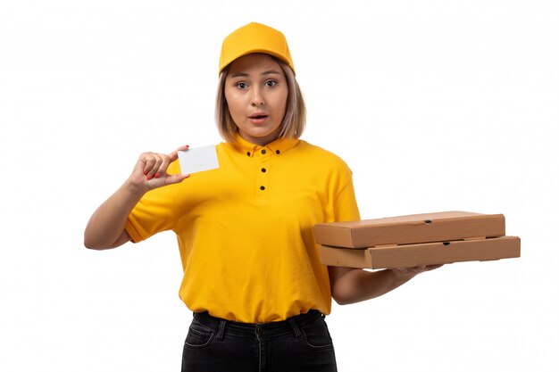 Un corriere femminile di vista frontale in protezione gialla della camicia gialla e jeans neri che tengono le scatole sull'alimento bianco della pizza di servizio del fondo