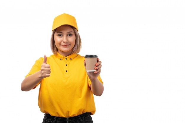 A front view female courier in yellow shirt yellow cap and black jeans holding coffee and smiling on white