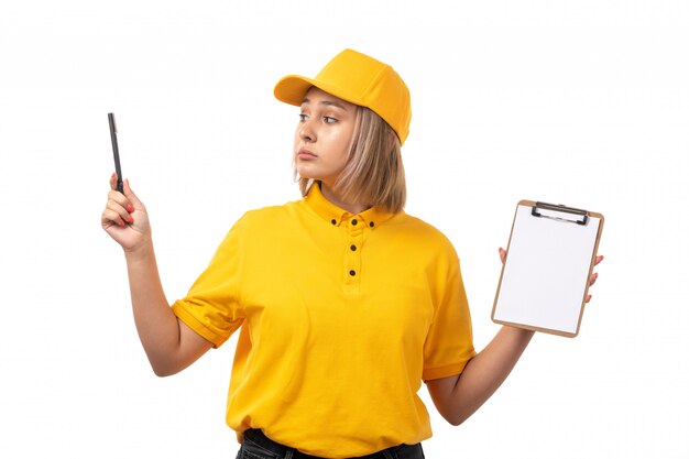 A front view female courier in yellow shirt yellow cap black jeans holding pen and paper on white