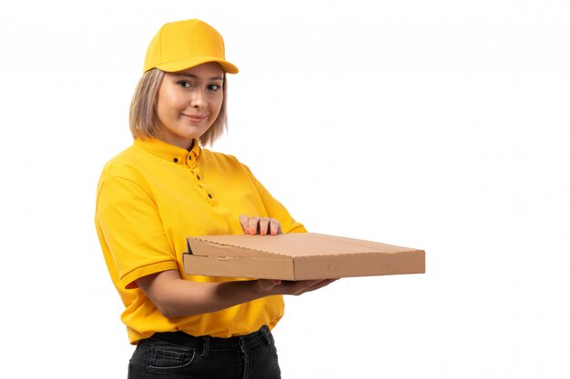 A front view female courier in yellow shirt yellow cap and black jeans holding pizza box on white