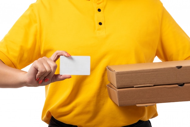 A front view female courier in yellow shirt yellow cap and black jeans holding pizza boxes and white card on white