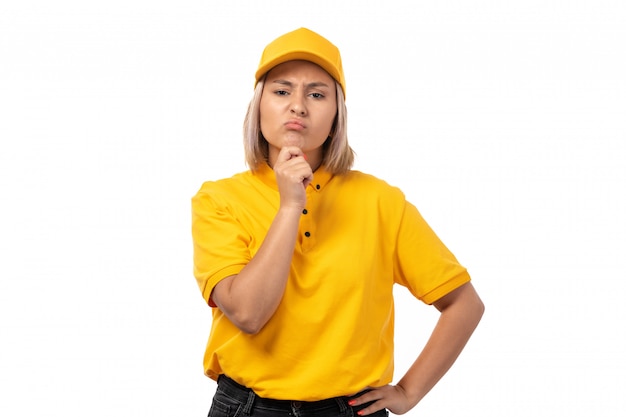 A front view female courier in yellow shirt yellow cap and black jeans posing thinking on white