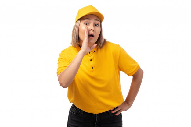 黄色のシャツの黄色のキャップと黒のジーンズが白のささやきのポーズで正面の女性宅配便