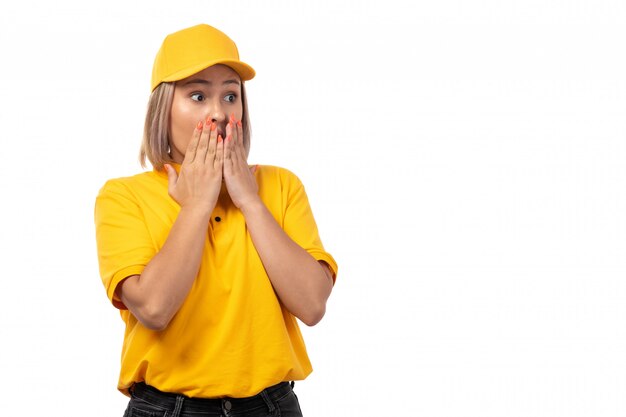 A front view female courier in yellow shirt yellow cap and black jeans posing with shocked expression on white