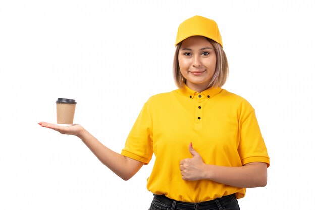 A front view female courier in yellow shirt yellow cap and black jeans smiling holding coffee cup on white