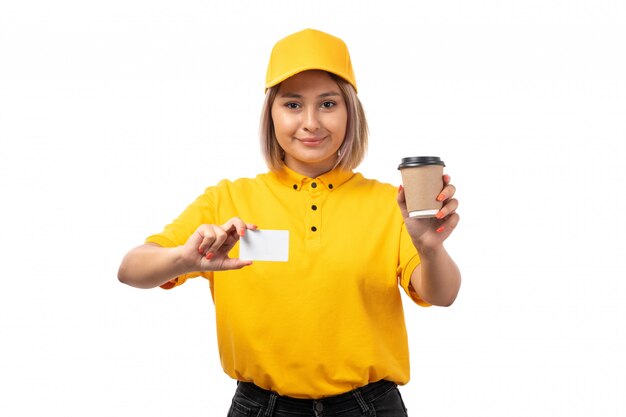 A front view female courier in yellow shirt yellow cap and black jeans smiling holding coffee cup on white