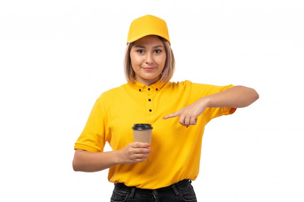 A front view female courier in yellow shirt yellow cap and black jeans smiling holding coffee cup on white