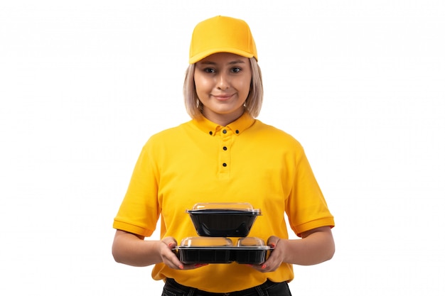 A front view female courier in yellow shirt yellow cap holding bowls with food smiling on white