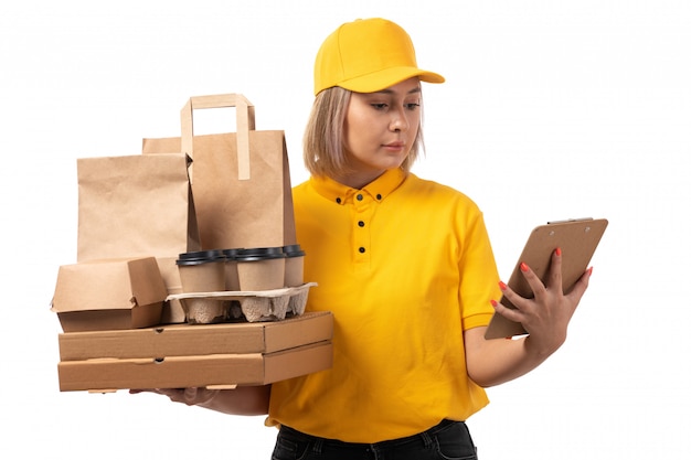 A front view female courier in yellow shirt yellow cap holding boxes coffee paper on white