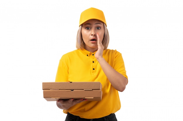 A front view female courier in yellow shirt yellow cap holding boxes on white