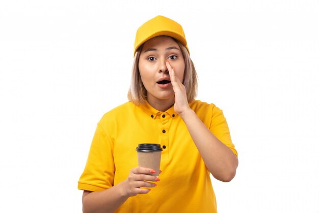 A front view female courier in yellow shirt yellow cap holding coffee cup on white