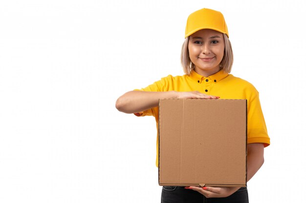 A front view female courier in yellow shirt yellow cap holding package smiling on white