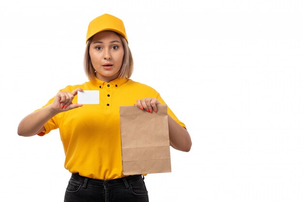 A front view female courier in yellow shirt yellow cap holding white card and package with food smiling on white