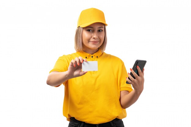 A front view female courier in yellow shirt yellow cap holding white card and smartphone on white