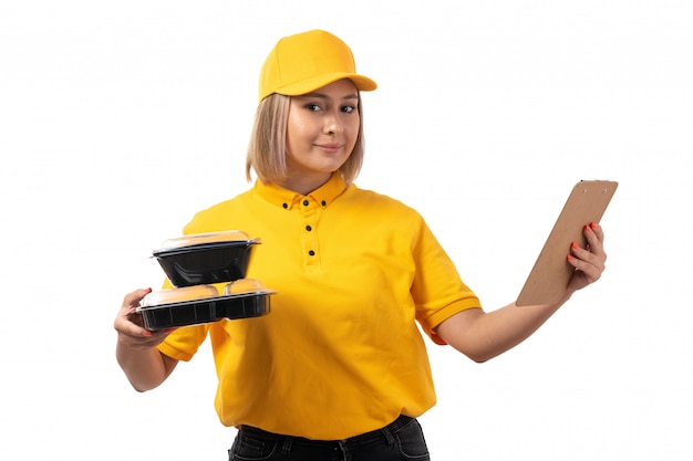 A front view female courier in yellow shirt yellow cap smiling holding bowls with food and paper on white