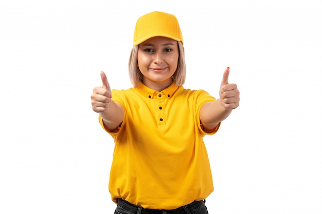 A front view female courier in yellow shirt yellow cap smiling showing like sign on white