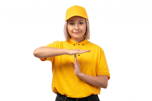 A front view female courier in yellow shirt yellow cap smiling showing t word on white