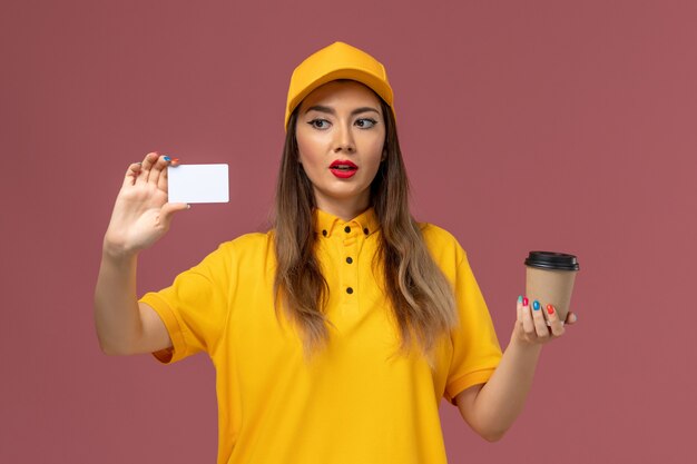 黄色のユニフォームと配達コーヒーカップと白いカードを保持しているキャップの女性の宅配便の正面図