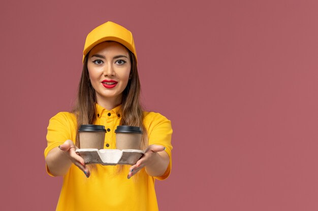 분홍색 벽에 배달 커피 컵을 들고 노란색 유니폼과 모자에 여성 택배의 전면보기