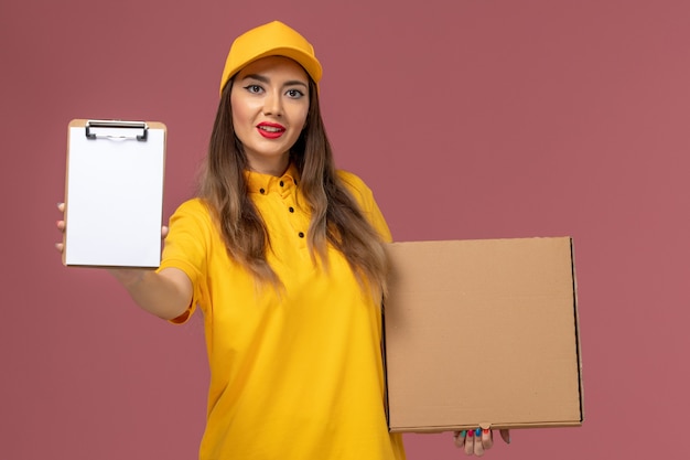 노란색 유니폼과 모자 분홍색 벽에 음식 상자와 메모장을 들고 여성 택배의 전면보기