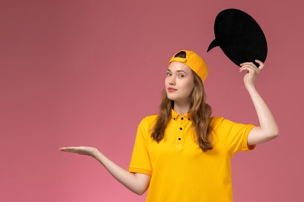 ピンクの壁のサービス提供制服会社に黒い看板を保持している黄色の制服と岬の正面図女性宅配便