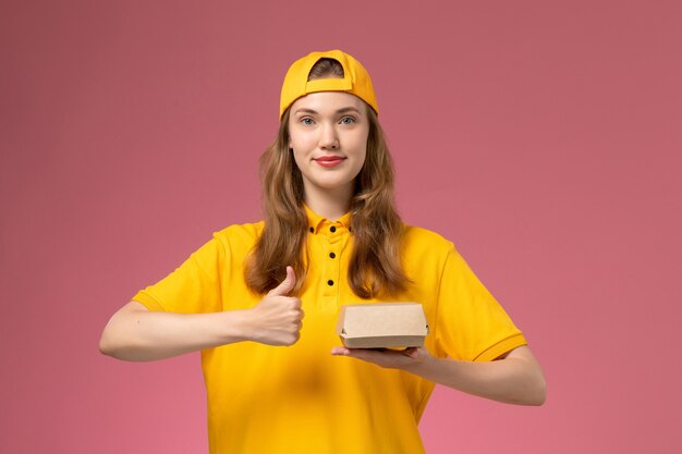 노란색 유니폼과 케이프 핑크 벽 서비스 배달 유니폼 회사 작업에 배달 음식 패키지를 들고 전면보기 여성 택배