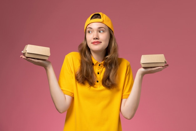 노란색 유니폼과 케이프 라이트 핑크 벽 서비스 작업 작업 배달 유니폼에 작은 배달 음식 패키지를 들고 전면보기 여성 택배