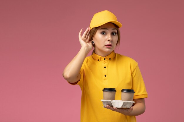 ピンクの背景にコーヒーカップを保持している黄色の制服黄色のケープの正面図女性宅配便制服配達作業の仕事