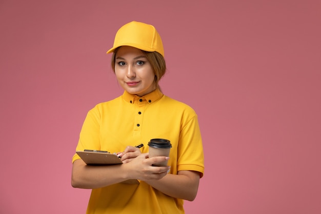 분홍색 배경 균일 한 배달 작업 작업 색상에 커피와 메모장을 들고 노란색 유니폼 노란색 케이프에서 전면보기 여성 택배