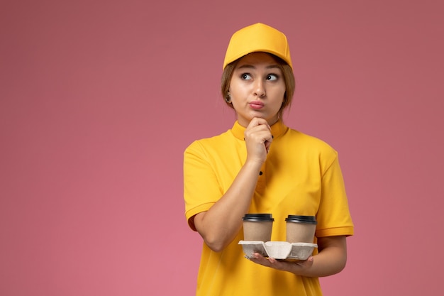 분홍색 배경 유니폼 배달 작업 작업에 생각 식으로 커피를 들고 노란색 유니폼 노란색 케이프에서 전면보기 여성 택배