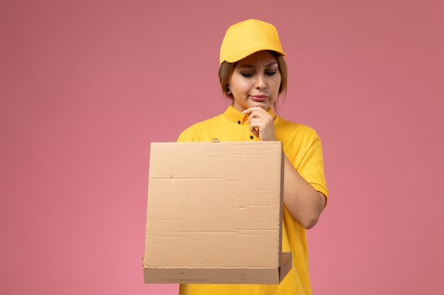 ピンクの背景に配達パッケージを保持している黄色の制服黄色の岬の正面図女性宅配便制服配達仕事の仕事