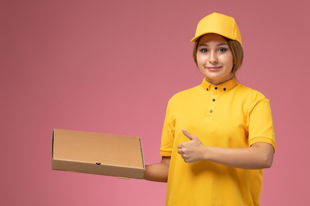 Front view female courier in yellow uniform yellow cape holding delivery package on pink background uniform delivery work job