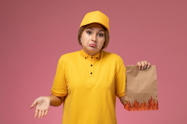 ピンクの背景に食品パッケージを保持している黄色の制服黄色のケープの正面図女性宅配便制服配達作業色