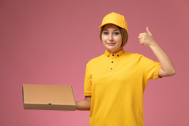 Front view female courier in yellow uniform yellow cape holding food package on the pink background uniform delivery work job