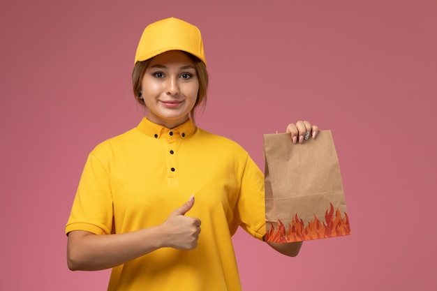 ピンクの机の上の食品パッケージを保持している黄色のユニフォーム黄色のケープの正面図女性宅配便