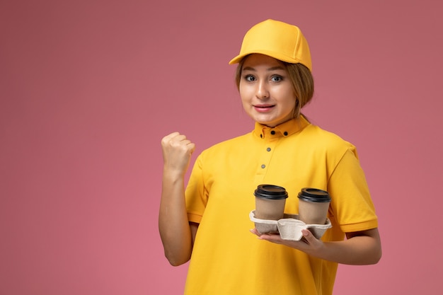 Front view female courier in yellow uniform yellow cape holding plastic coffee cups on the light background uniform delivery work job color