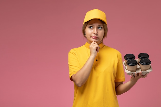 분홍색 배경 유니폼 배달 작업 색상 작업에 생각 플라스틱 커피 컵을 들고 노란색 유니폼 노란색 케이프 전면보기 여성 택배