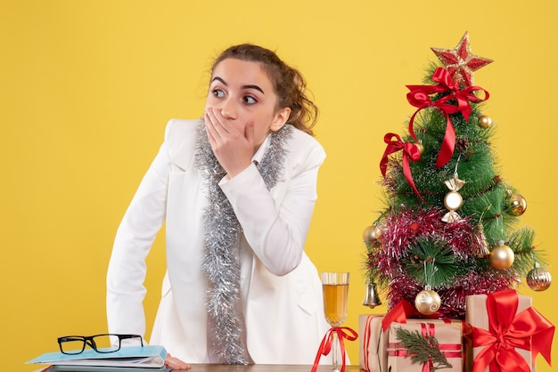 Вид спереди женщина-врач вокруг рождественских подарков и елки с потрясенным лицом
