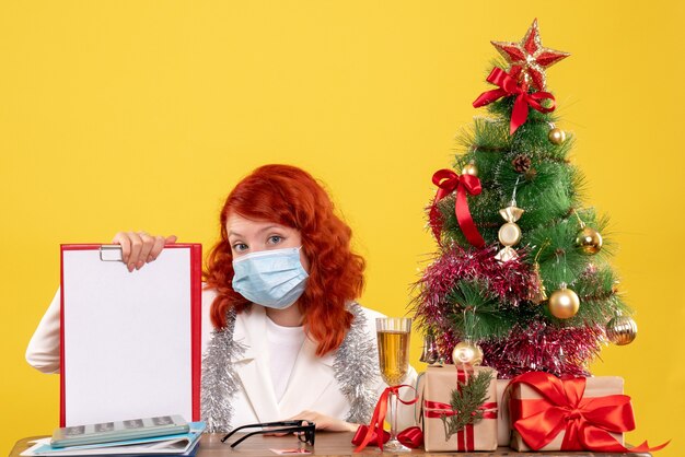 Front view female doctor around xmas tree and presents sitting in mask